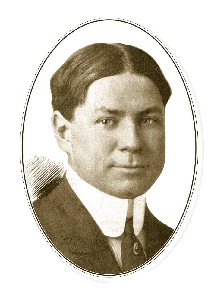 Portrait of a light-skinned man with medium length hair parted straight down the middle. He is wearing a dark suit jacket and tie, and his white collard shirt has a very tall collar.