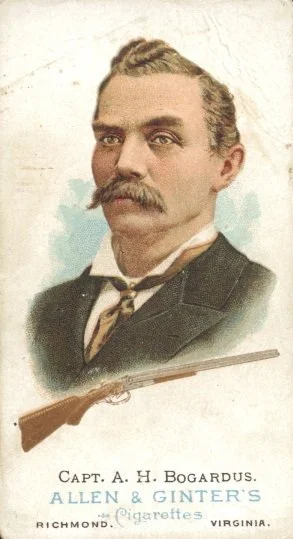illustration of a light skinned man with short wavy light colored hair and a long, thick mustache. A rifle is pictured along the bottom of the image along with the words