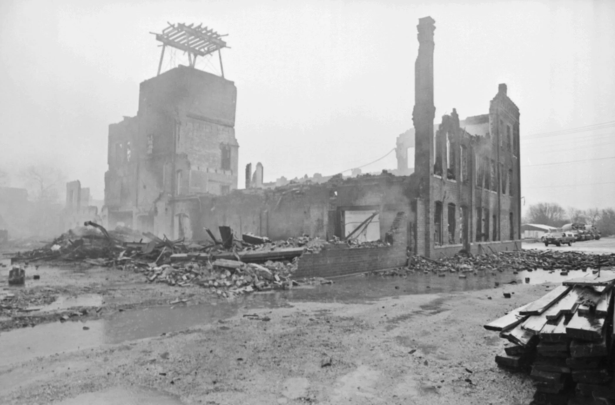 through the haze there is a crumbled brick building, some fascade still stands but most of the brick building is rubble on the ground.